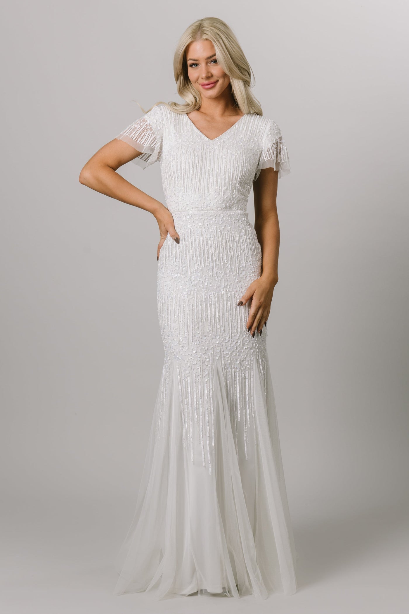 Modest wedding dress with flutter sleeves and v-neckline. It is a fitted dress with sequin beading. This Moments Made Bridal dress is stunning on any body type.