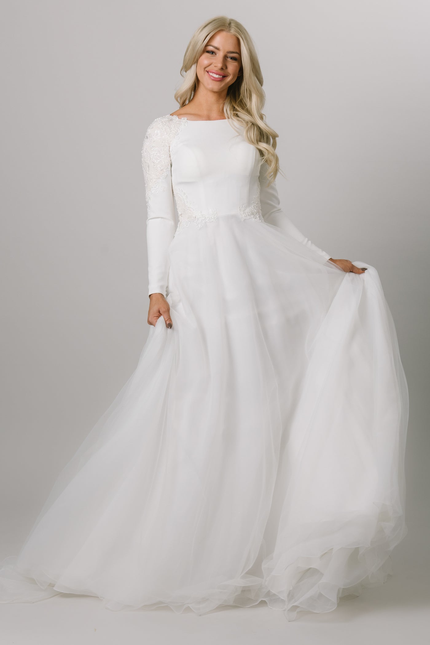 Moments Made Bridal wedding dress with long sleeves. This modest wedding dress has a high scoop neckline and a-lin fit. This is a perfect wedding dress for those cooler months. It has a zipper covered by buttons down the back.