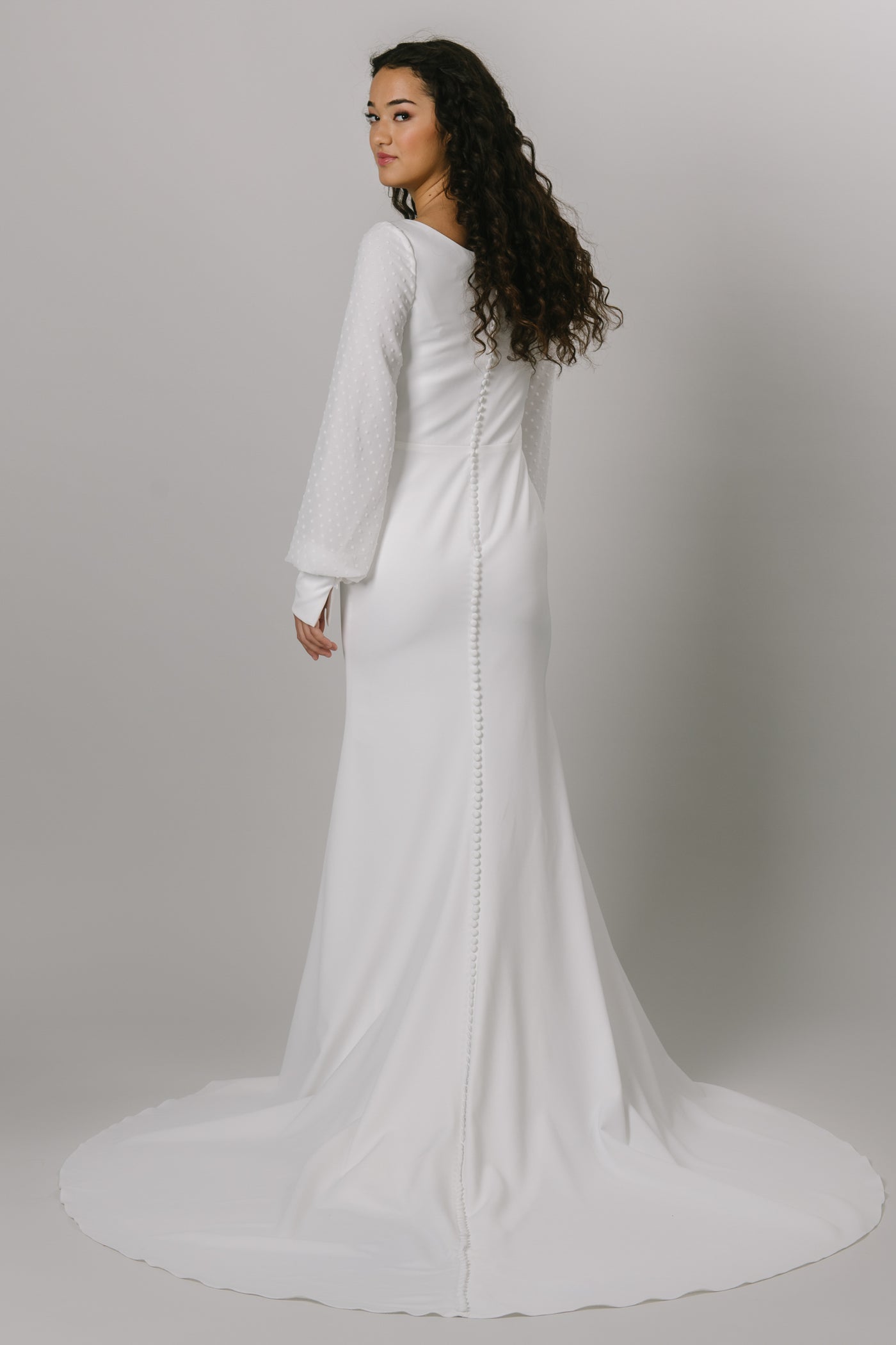 Back shot of our beautiful modest wedding dress with a simple crepe fabric and pattern. The long bishop sleeves have a beautiful swiss dot pattern.