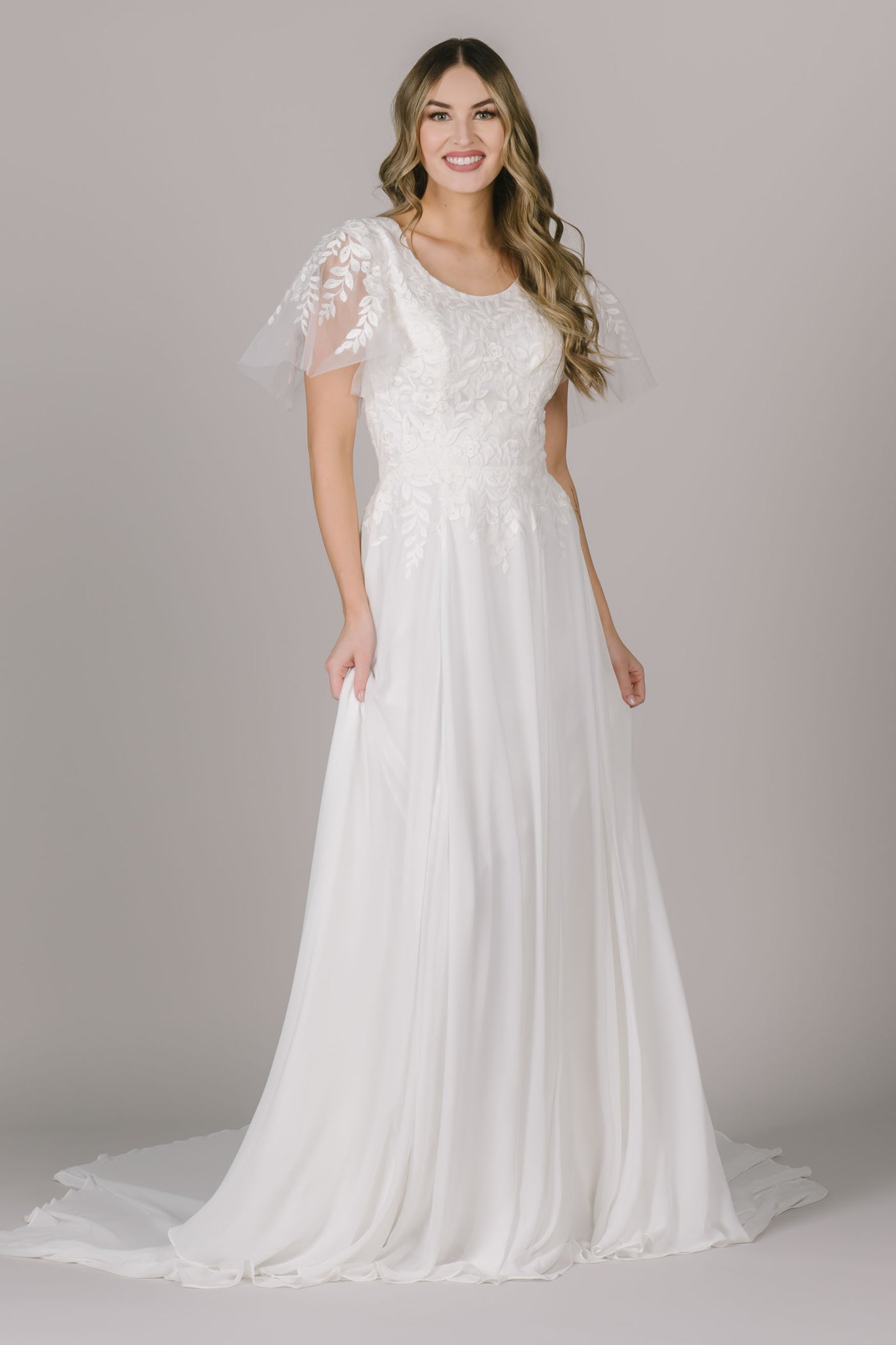 A modest wedding dress in Utah features beautiful falling lace throughout the sleeves and bodice of the dress, a scoop neck, and a-line silhouette that flatters every body type!