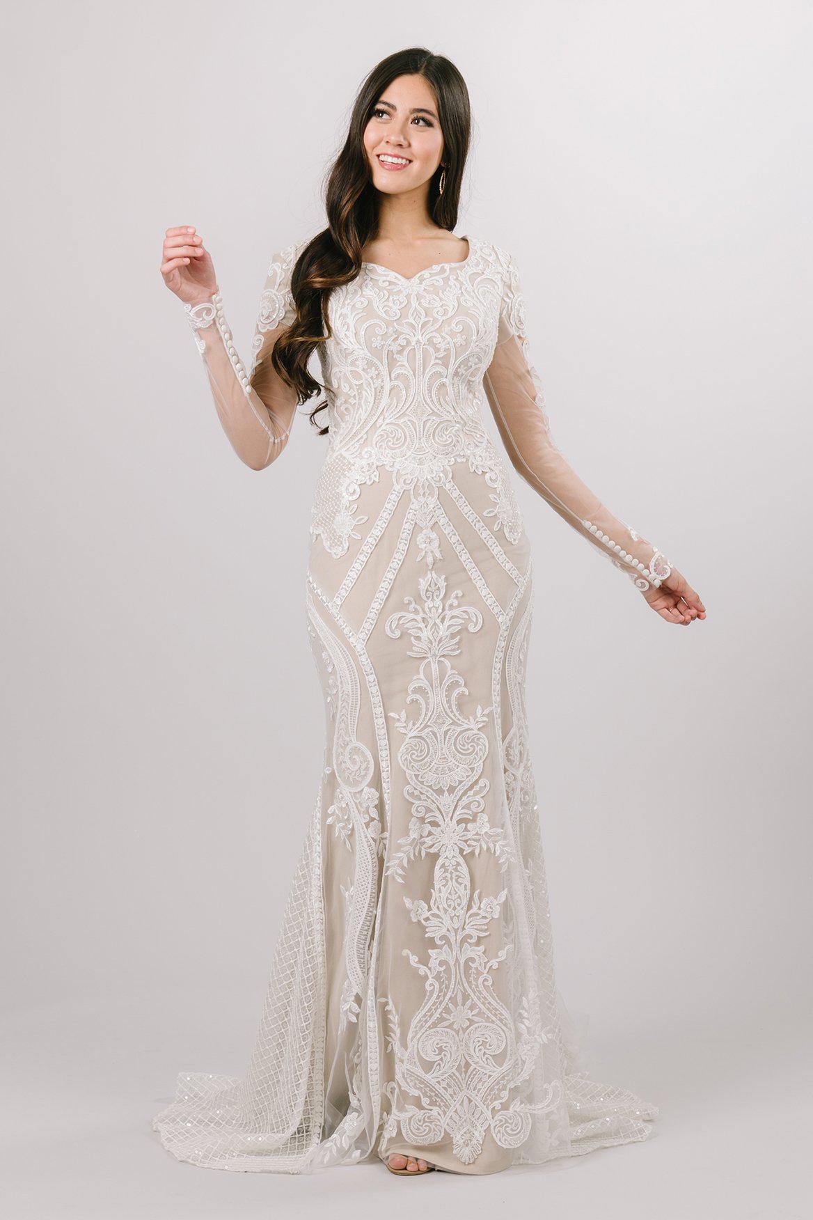 Modest wedding dress with long sleeves. It has a heart shaped neckline and fitted silhouette. It has lace detailing covering the whole dress. It has buttons on the sleeves. 