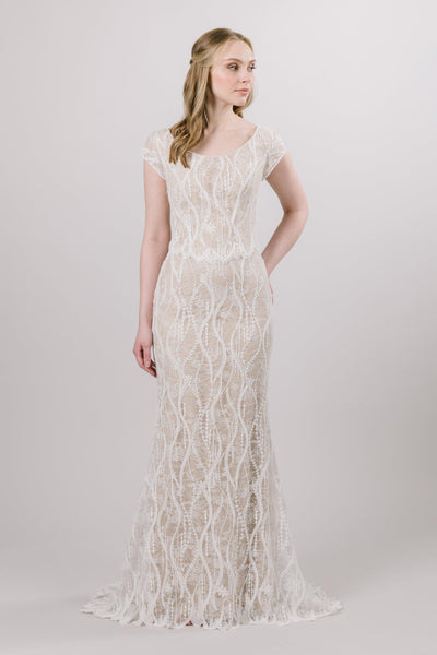 Chantilly embroidered lace cascades vertically down the entire sheath silhouette of this modest wedding dress, elongating the figure flawlessly.