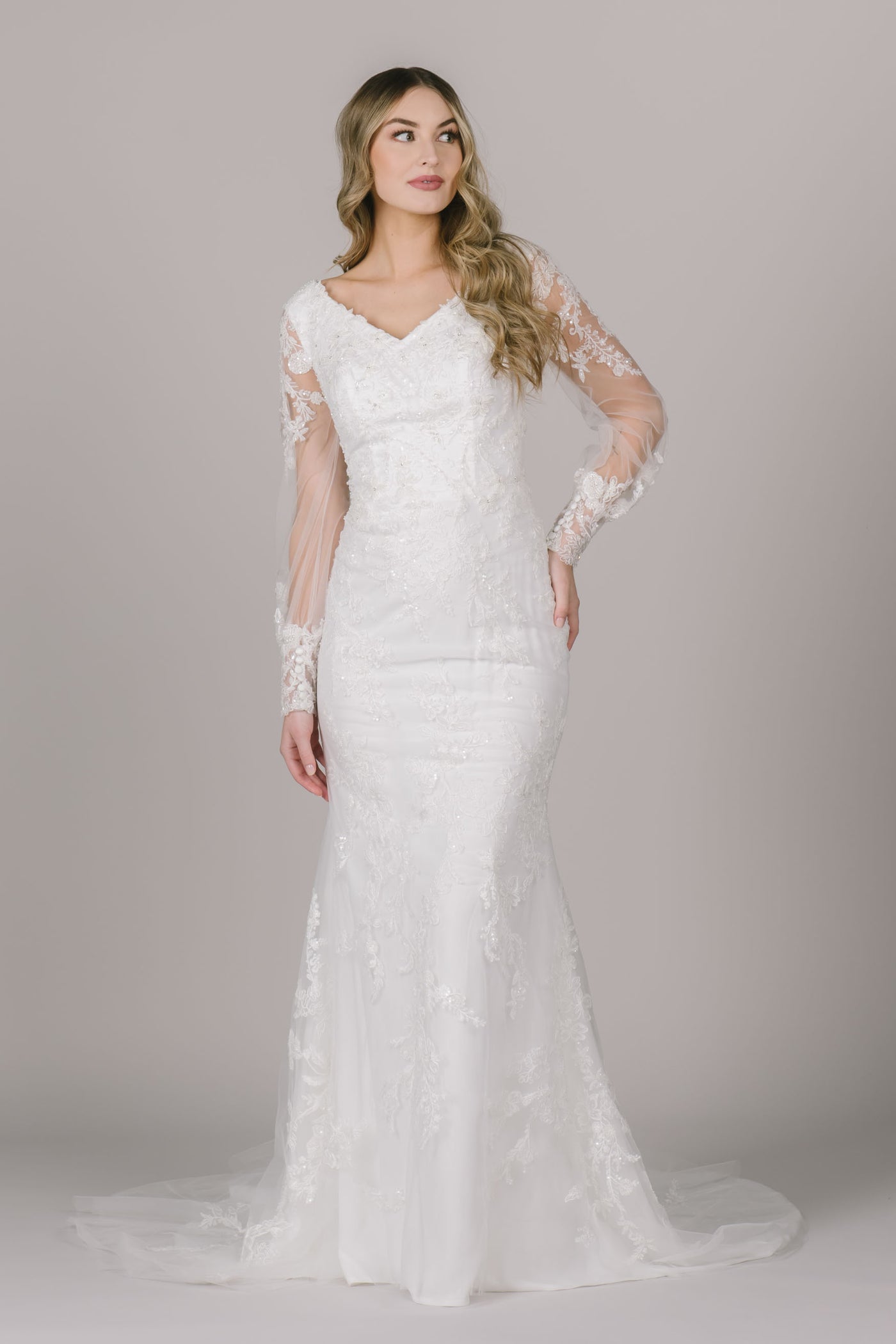 A picture of a fitted modest wedding dress with a beautiful beaded lace detail, v-neckline, and bishop sleeves