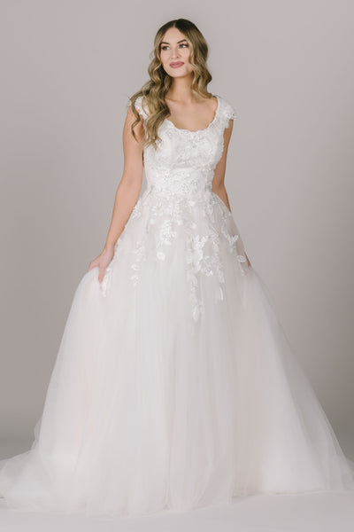 The Ophelia is a modest wedding dress in Utah with beautiful floral lace applique, cap sleeves, and a wide scoop neckline.