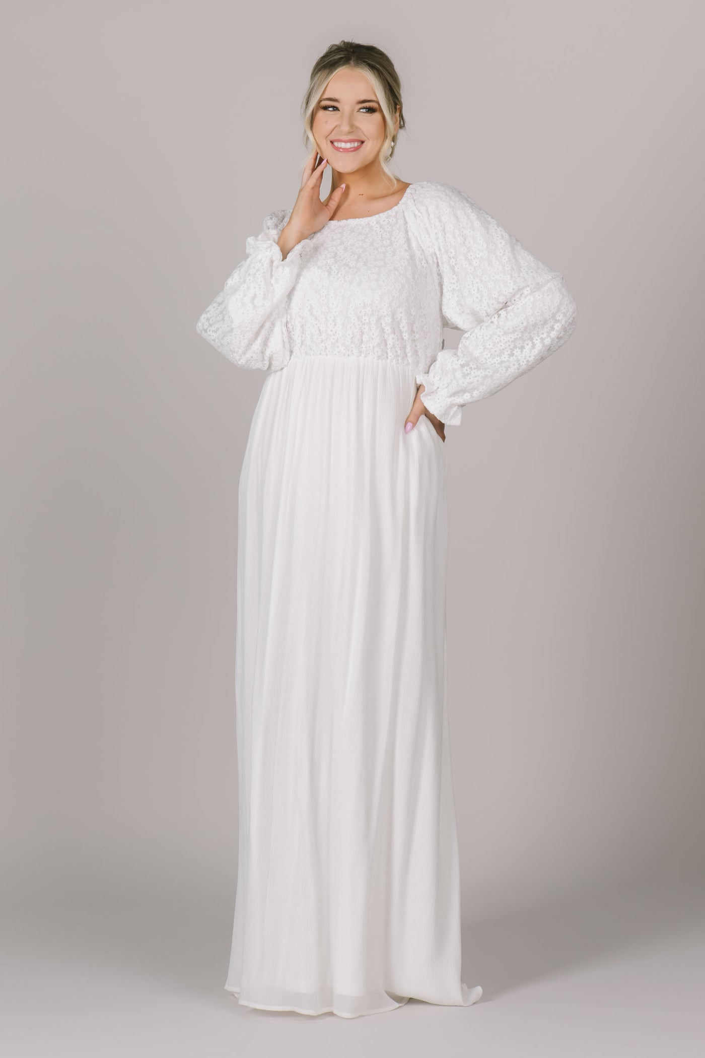 An LDS modest temple dress with a cinched waistband, bishop sleeves with a cinched cuff, and scoop neckline. The bodice is made of a stunning floral lace.