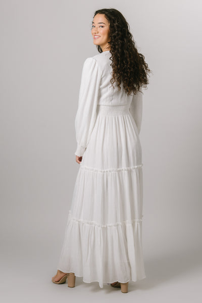 Back shot of our modest, smocked, tiered white maxi dress with long bishop sleeve and a v-neck.
