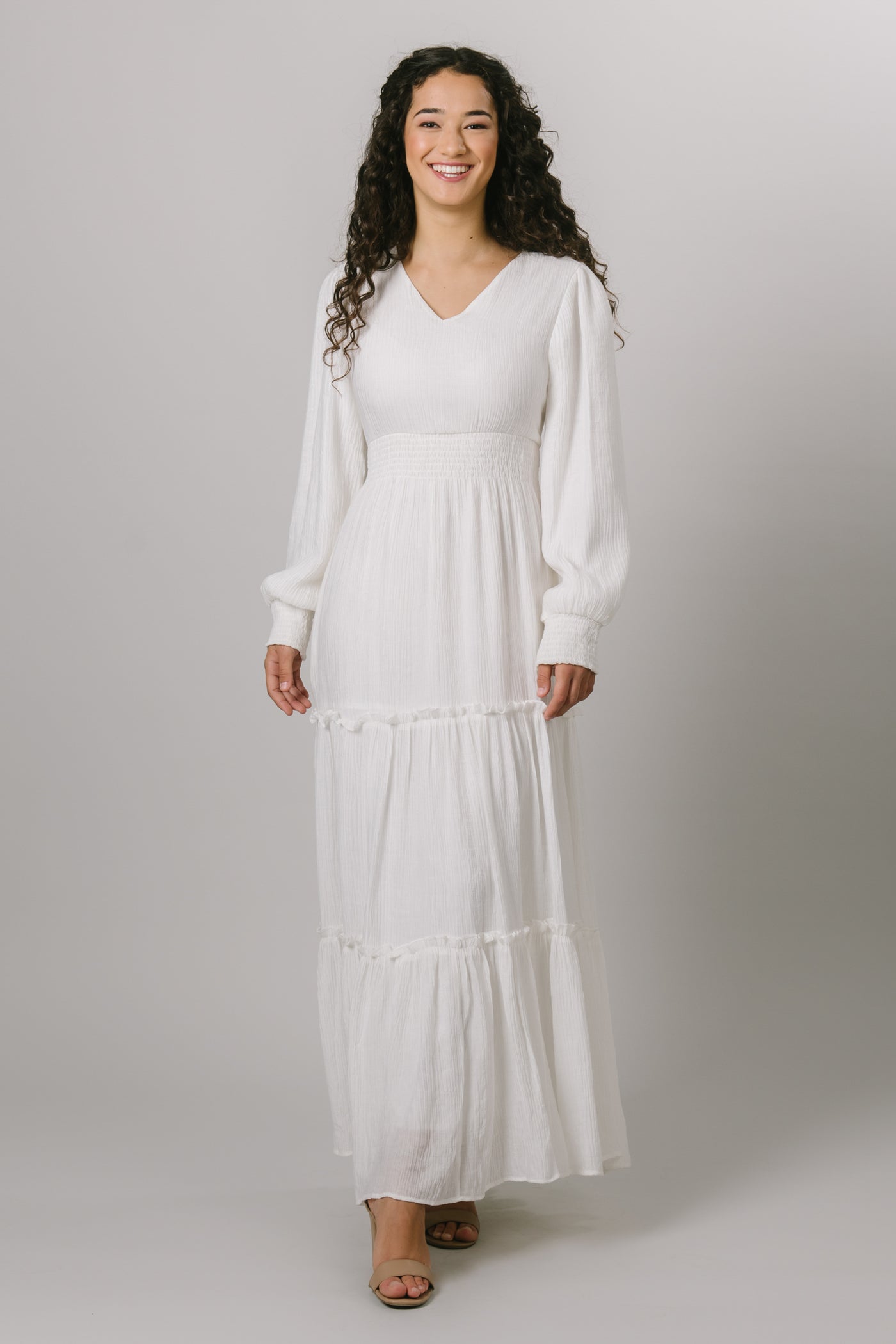 A modest smocked, tiered white maxi dress with long bishop sleeve and a v-neck.