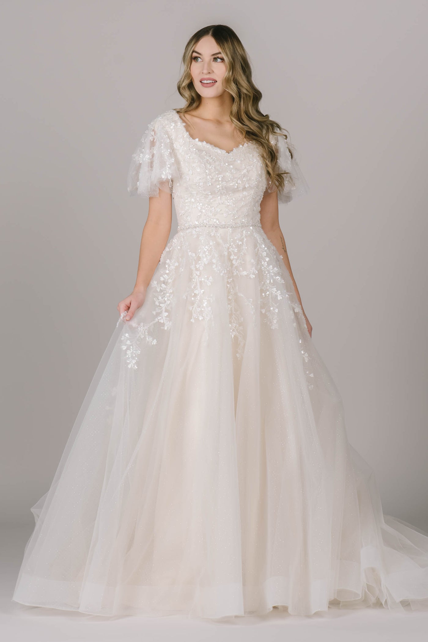 This is one of our favorite new modest wedding dresses! It has a stunning lace all throughout the dress, a square v-neckline, and gorgeous flutter sleeves.