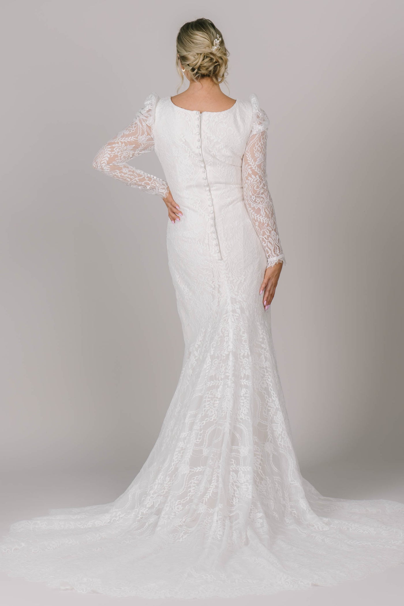 A back angle of this fitted modest wedding dress that is covered in lace, has buttons down the back, and has the most stunning train!