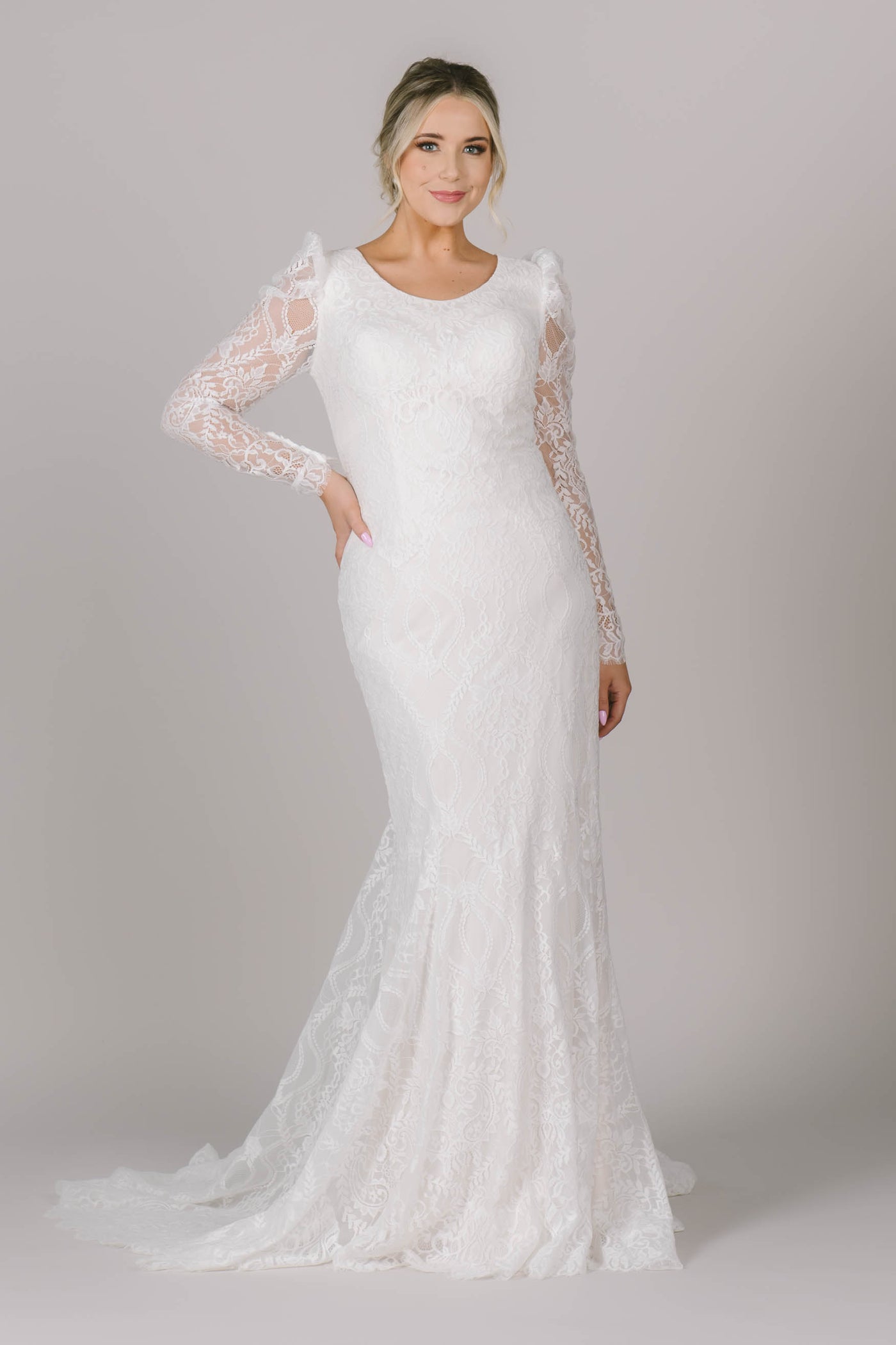 A front angle of a modest wedding dress that features a fitted silhouette, scoop neck, and the most perfect long sleeves. The lace on this gown is stunning!