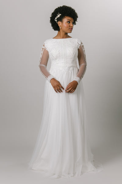 This modest wedding dress includes a high neck line, sheer long sleeves, a flowy tool skirt, and a beaded and lace bodice.