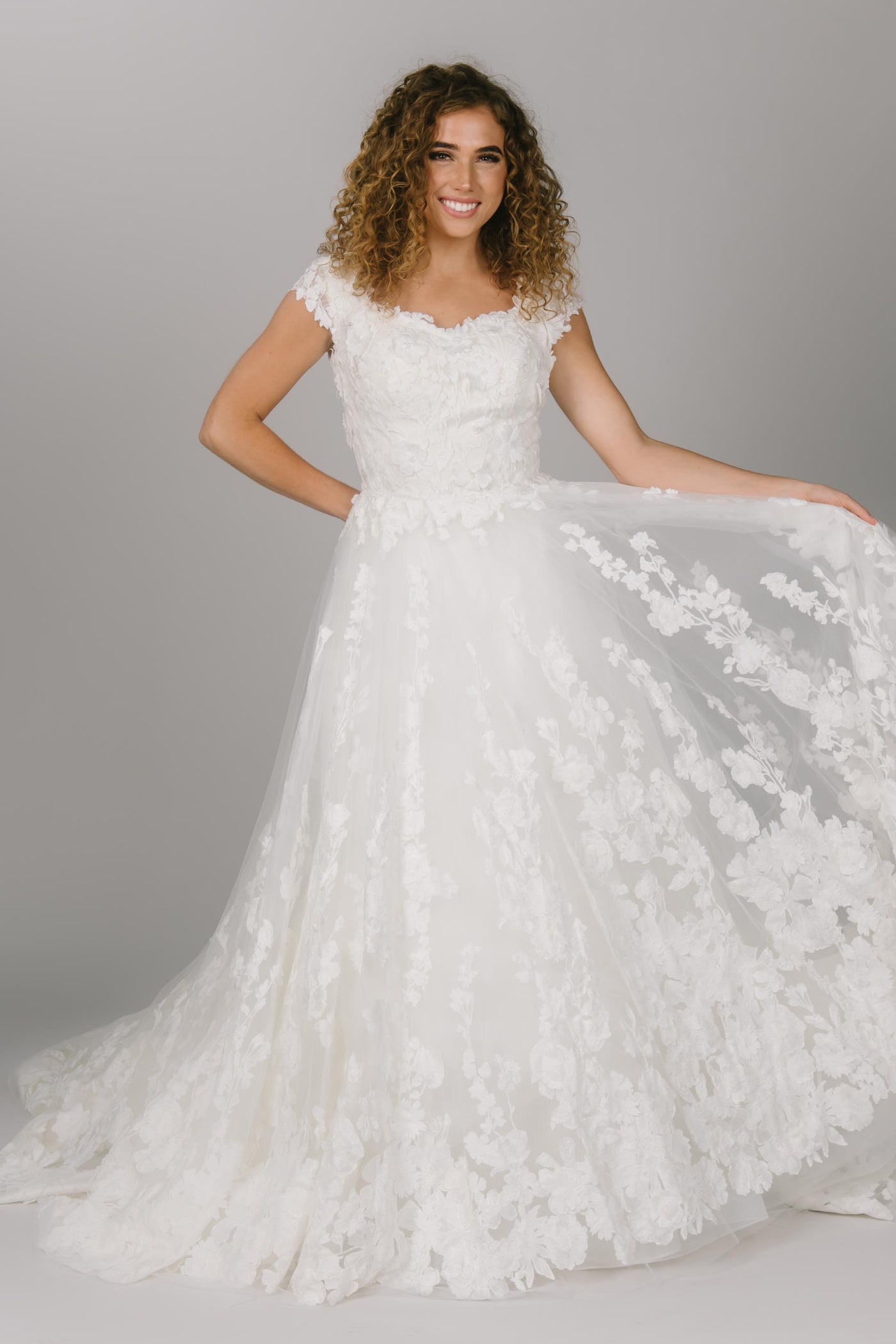 Overskirt view of modest wedding dress that is fitted. It has a sweetheart neckline and cap sleeves. The 3D sheet lace covers the dress. This is the ultimate fitted modest wedding dress.