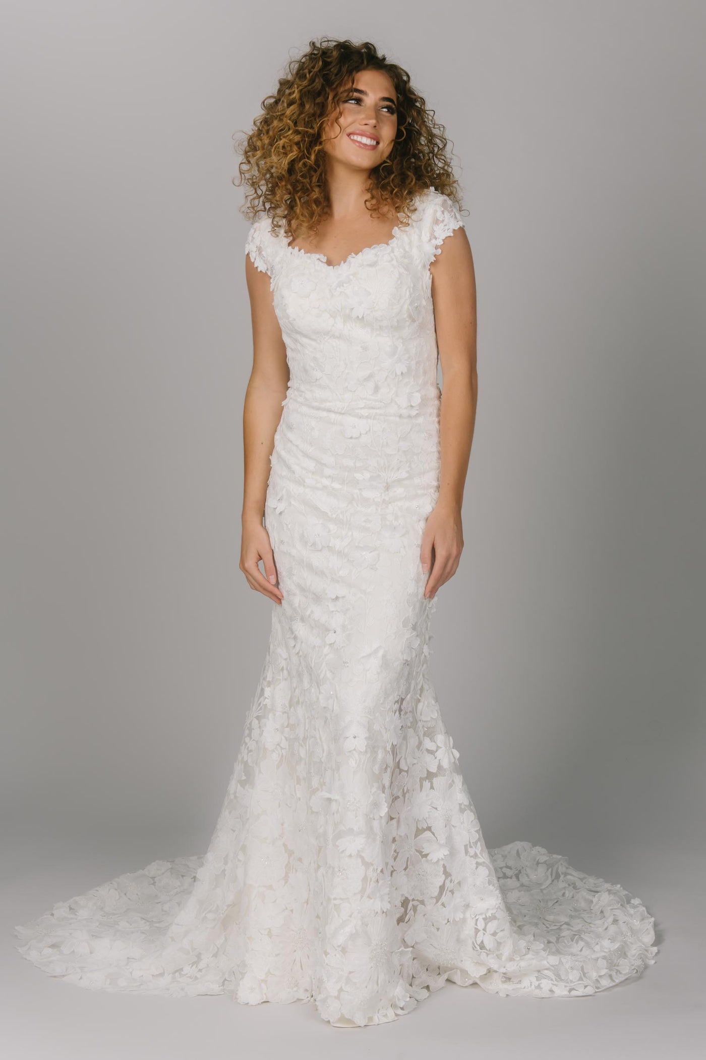 Front view of modest wedding dress that is fitted. It has a sweetheart neckline and cap sleeves. The 3D sheet lace covers the dress. This is the ultimate fitted modest wedding dress. 