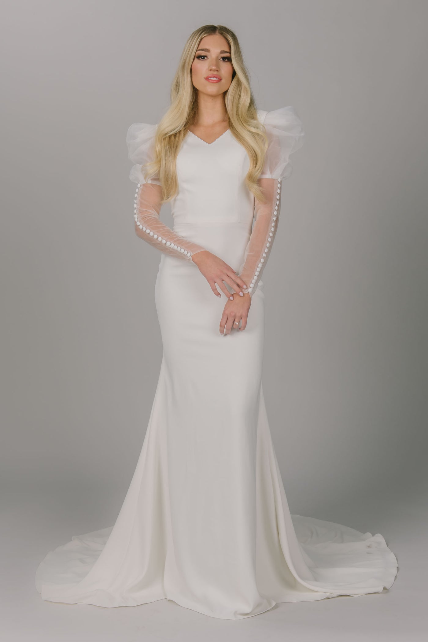 A front shot of a modest wedding dress with a v-neck, long puff sleeves, and a fitted silhouette.