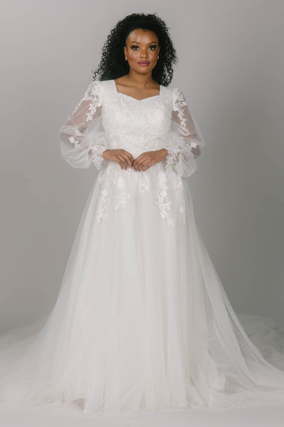 Front view of modest wedding dress, featuring lace bishop sleeves. It has a sweetheart neckline and tulle skirt. It has leaf-like lace that covers the sleeves and top of the dress. The Benny dress is the perfect a-line modest wedding dress.  