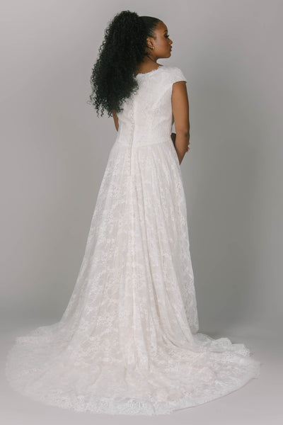 Complete lace modest wedding dress with scoop neckline. This dress is a-line and has cap sleeves. It has a longer lace train and dipped waistline. This dress is perfect for the modest wedding dress woman who wants lace.
