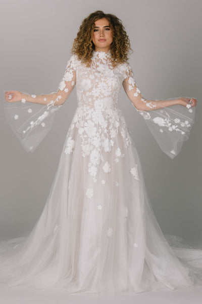 Front view of modest boho wedding dress. This dress is high neck and a-line. It has bell sleeves and 3D flower lace. Gorgeous modest wedding dress. 