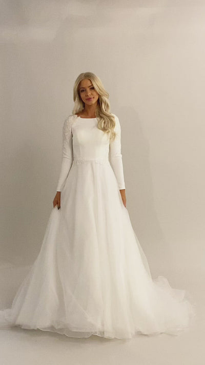 Video of Moments Made Bridal wedding dress with long sleeves. This modest wedding dress has a high scoop neckline and a-lin fit. This is a perfect wedding dress for those cooler months. It has a zipper covered by buttons down the back.