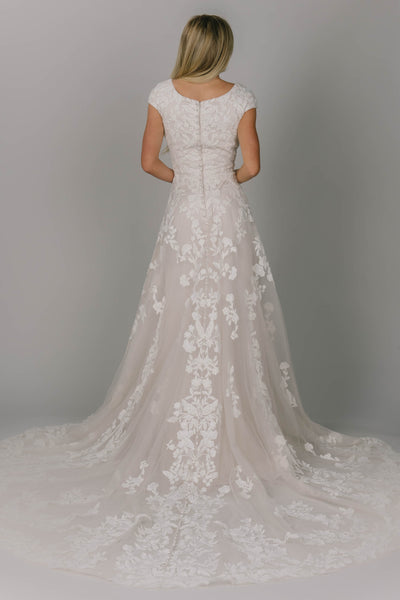 Modest wedding dress featuring an a-line fit and v-neckline. It has flower lace all over the dress but more on the top. Covered buttons go all the way down the back of the dress.
