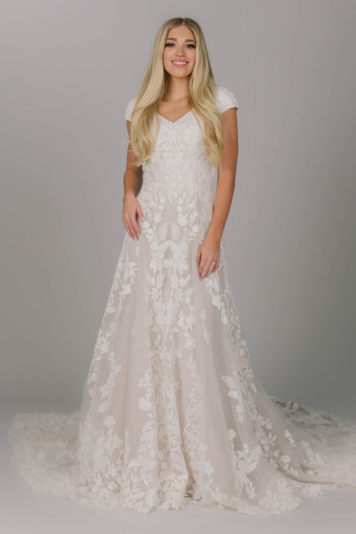 Modest wedding dress featuring an a-line fit and v-neckline. It has flower lace all over the dress but more on the top. Covered buttons go all the way down the back of the dress.  