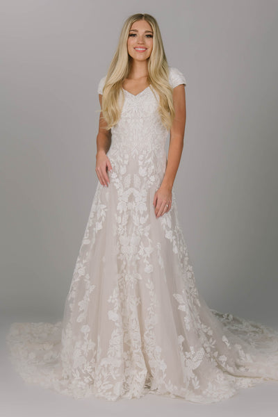 Modest wedding dress featuring an a-line fit and v-neckline. It has flower lace all over the dress but more on the top. Covered buttons go all the way down the back of the dress.  