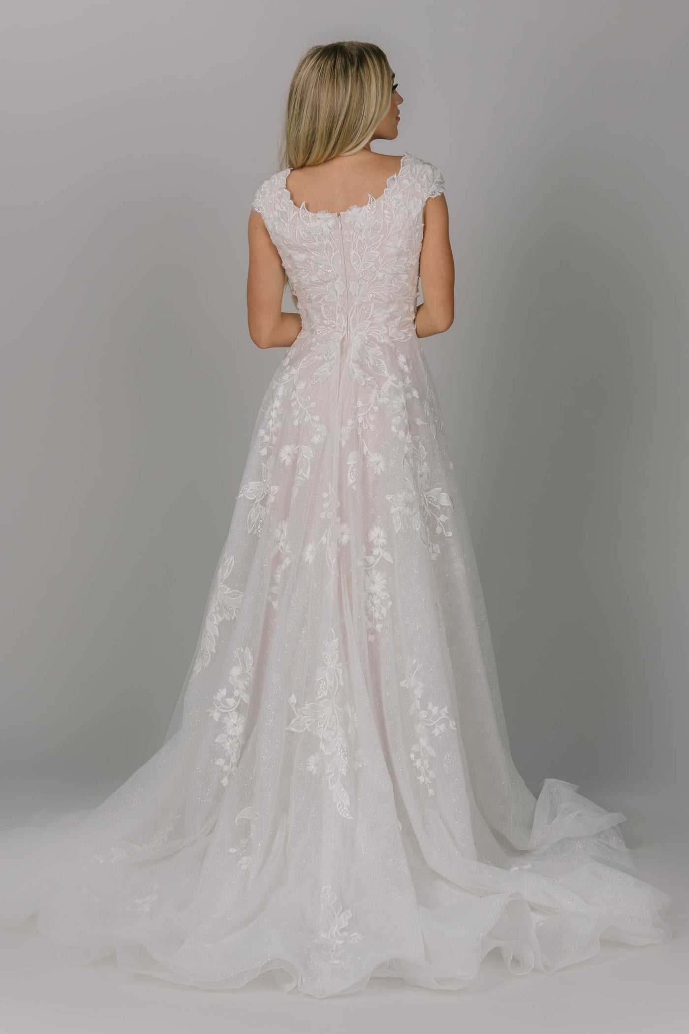 Glitter modest wedding dress. It has a scoop neckline and cap sleeves. The skirt has a soft sparkly glow. It has point leaf lace and a flowy train.