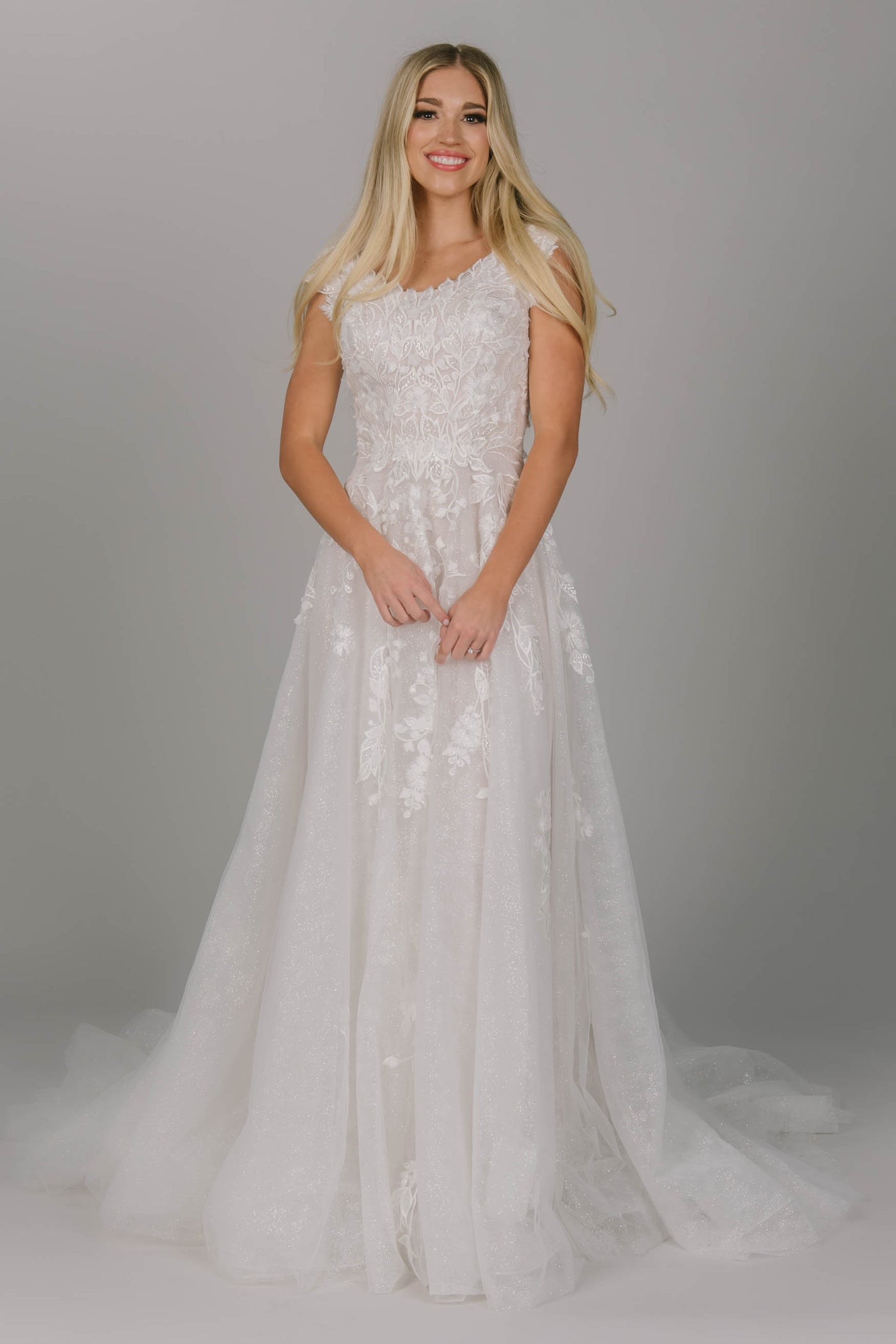 Glitter modest wedding dress. It has a scoop neckline and cap sleeves. The skirt has a soft sparkly glow. It has point leaf lace and a flowy train. 