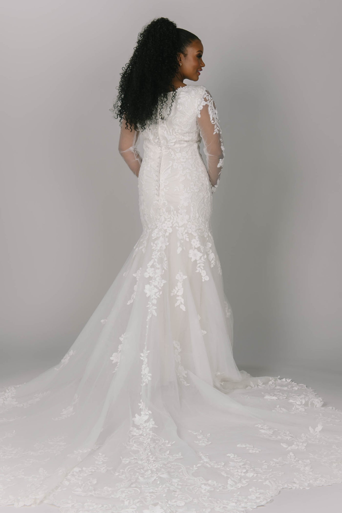 Back view of fitted modest wedding dress. This dress has flower/vine lace which creates a gorgeous lace train. It has long sleeves and a v-neckline.