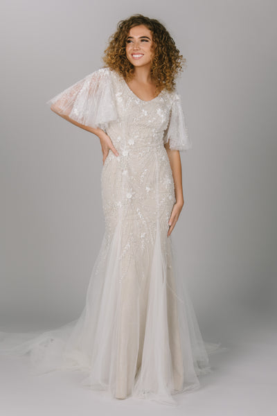 Front view of modest wedding dress with flutter sleeves. It has beading and lace. The tulle skirt and sleeves give it flow and movement. It is a gorgeous modest wedding dress.