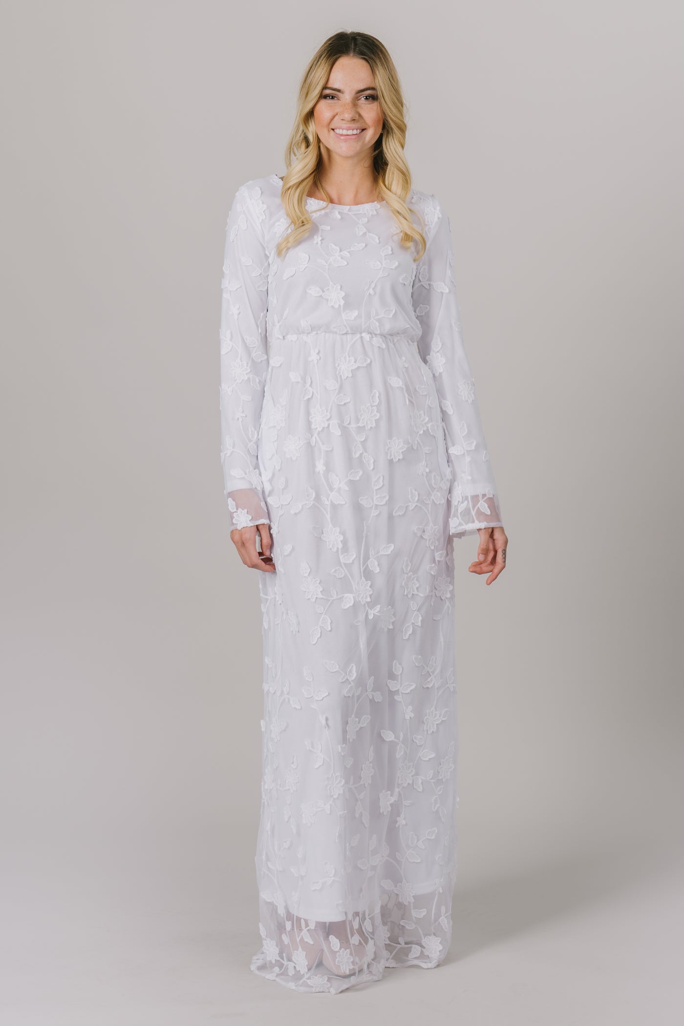 This LDS temple dress features a fully lined, floral lace with a cinched waistband and flowy long sleeves. It includes two pockets.