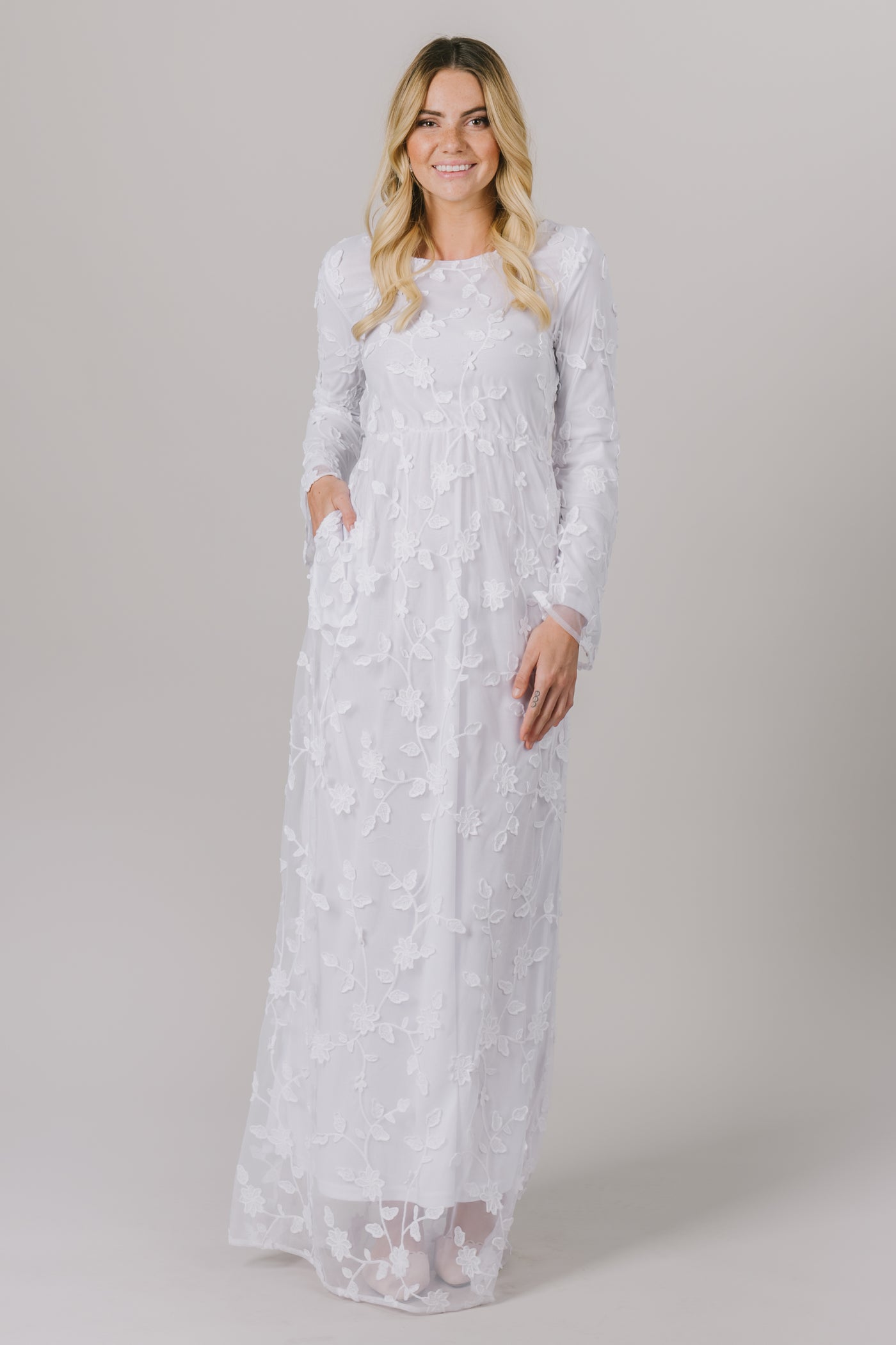 This LDS temple dress features a fully lined, lovely floral lace with a cinched waistband and gorgeous flowy long sleeves. It includes two functional pockets.