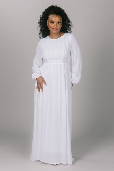 Front view of temple dress with a little bit of lace. It has vertical strips of lace on the top of the dress. It has a simple skirt and bishop styled sleeves. The high scoop neckline and pockets of this dress make it very efficient.
