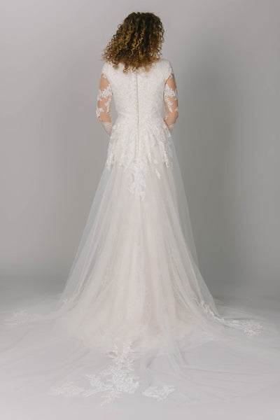 Back view of modest wedding dress with long sleeves. It has a v-neckline and long tulle train. The lace is soft and delicate and is found through the dress. This is a dreamy modest wedding gown.