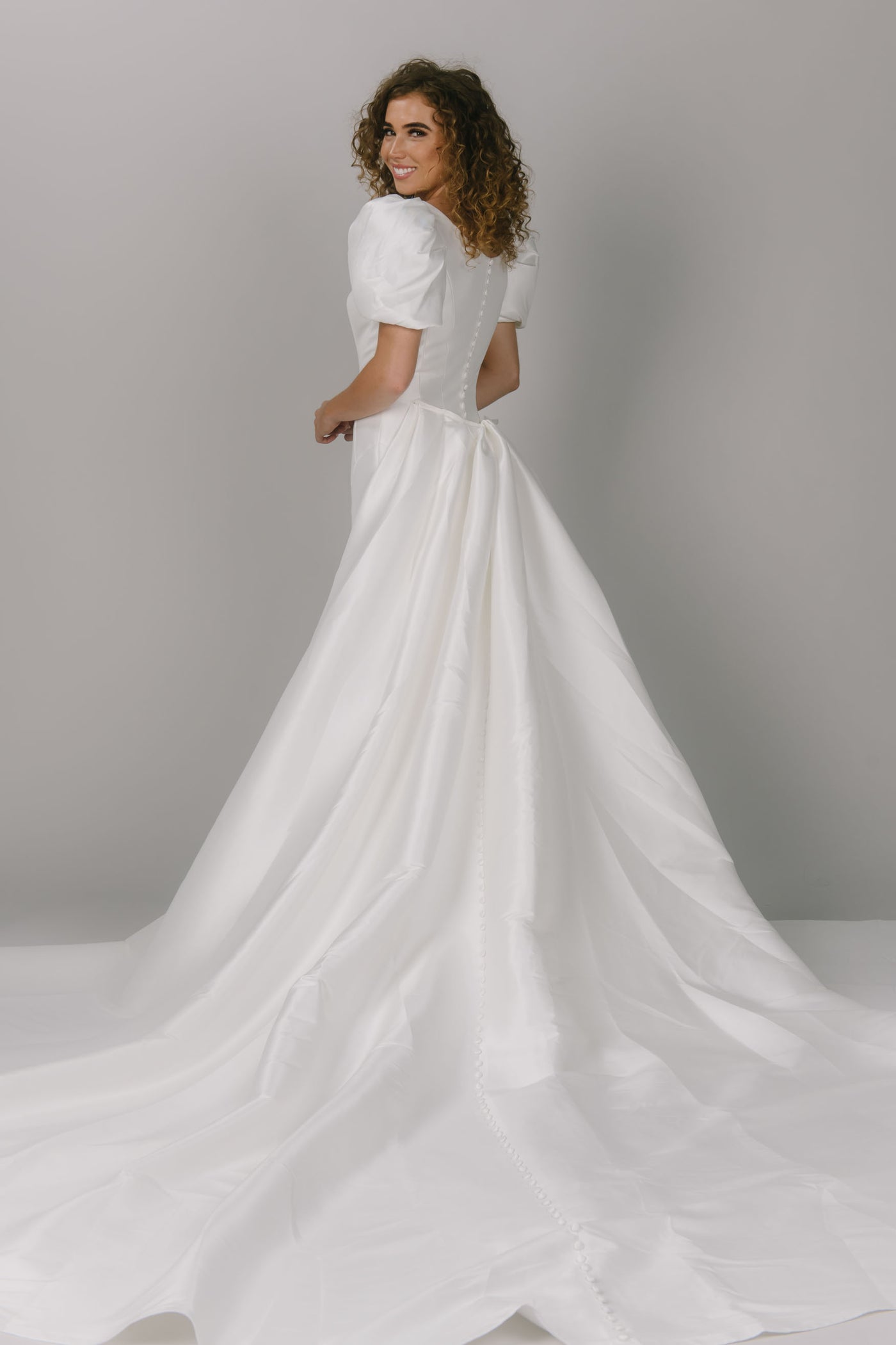 Back view with overskirt of modest wedding dress with contour lines. It is a fitted dress with puffed sleeves. This dress has a scoop neckline and is a gorgeous modest wedding gown.
