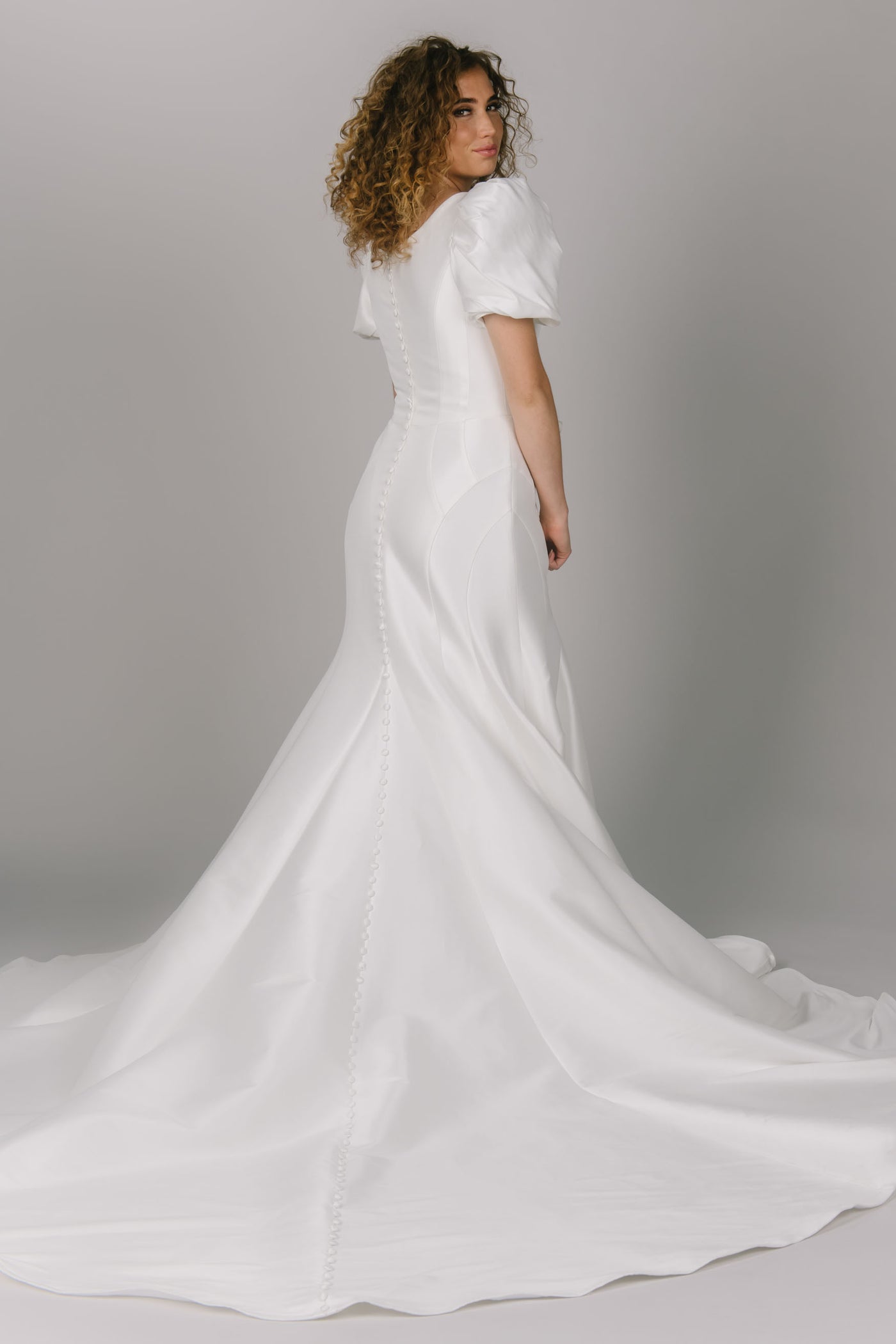 Back view of modest wedding dress with contour lines. It is a fitted dress with puffed sleeves. This dress has a scoop neckline and is a gorgeous modest wedding gown.