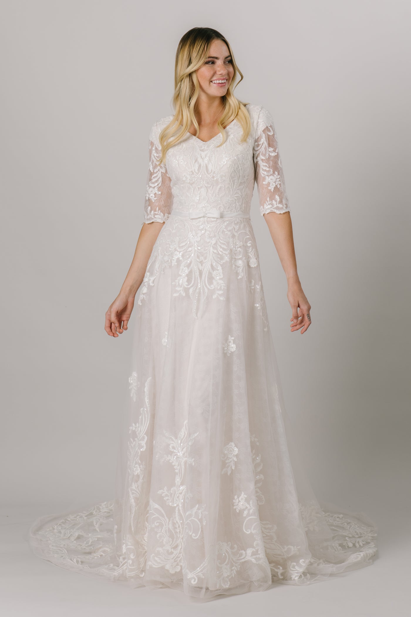 This modest wedding dress has a flattering a-line fit with an absolutely gorgeous lace pattern. With half sleeves and buttons down the back, how could we say no?  Style Love: Little belt with an adorable bow to accentuate the waist!