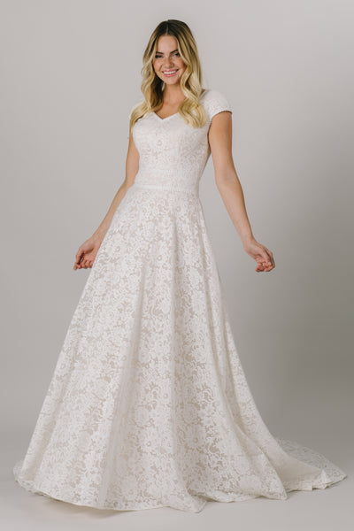 This modest wedding dress has a flattering fit somewhere between an a-line and a ballgown silhouette. It features a dainty full lace pattern and a v-neckline.  Available in Sand/Ivory (pictured) and Almond/Champagne/Ivory.