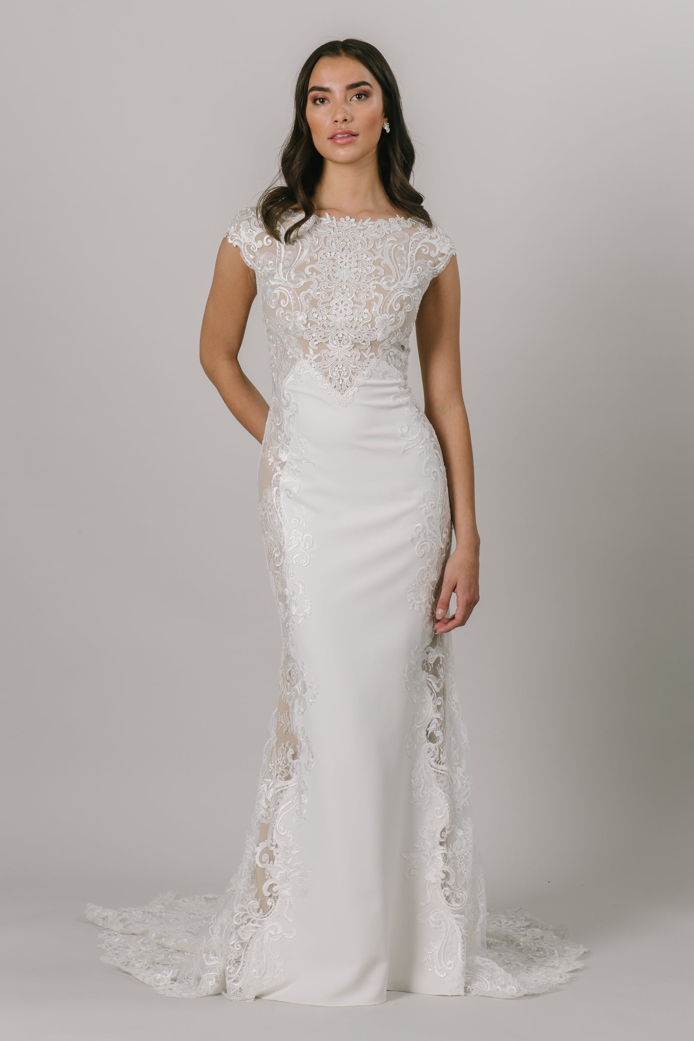 This fit-and-flare, modest wedding dress features gorgeous lace detailing at the top and own the sides of the dress. There are buttons down the back that add a darling compliment to the lace. Shown in Ivory/Nude/Ivory.  Style Love: Nude lining helps the lace pop!