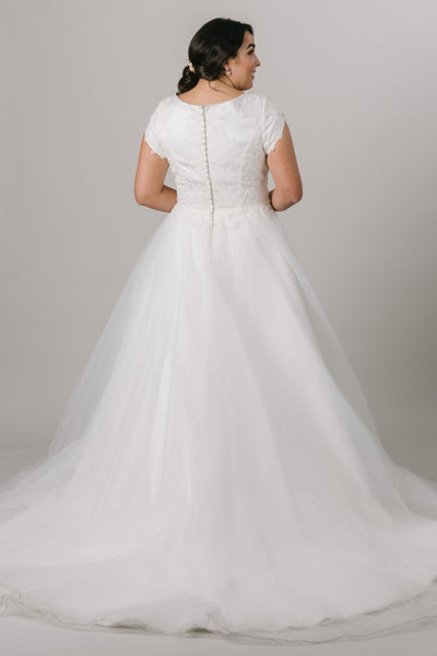 This elegant modest wedding dress is perfect for the traditional bride! We love the soft petal sleeves, the wide boat neckline, and the flattering cinched waist. The gown is shown in Ivory.  Style Love: Add a simple belt to add more sparkle to this gown or keep it simple as is! Feeling like a princess? Add a tiara to complete the look! From a Bridal store in downtown SLC,Utah.