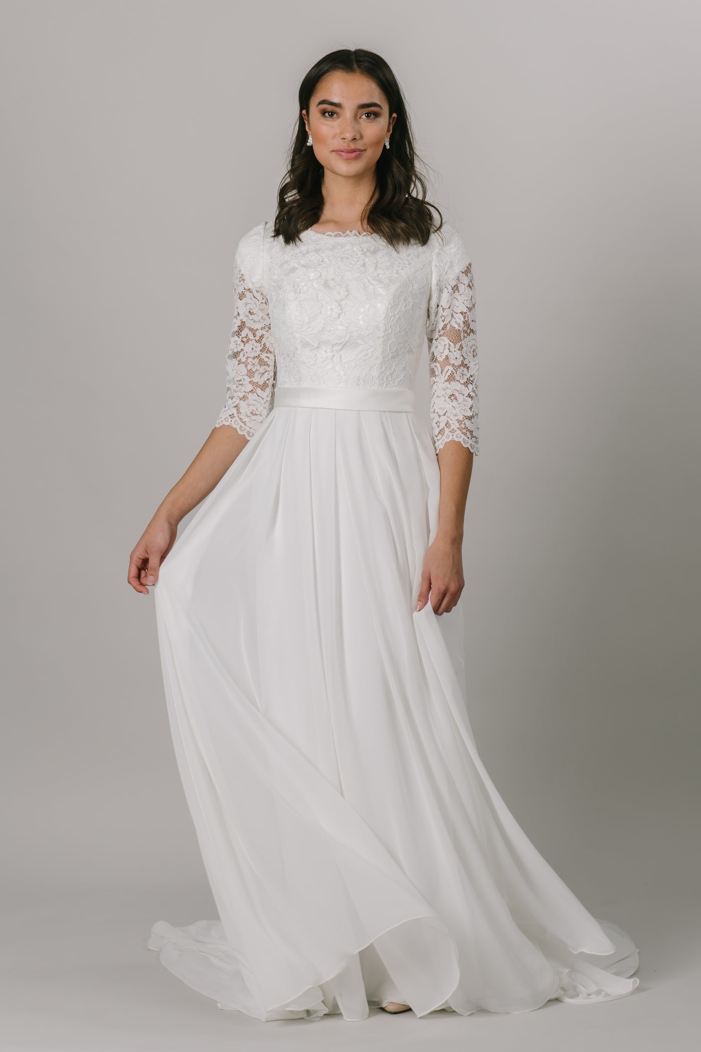 This classic modest wedding dress has everything you could want! Lace top, simple bottom, with 3/4 sleeve! The illusion sleeves, flattering waistband, and the pleated chiffon skirt make for the perfect dress. Almost a long sleeve with 3/4 sleeves. The gown is shown in ivory but is also available in white. Plus size available in the store.  Style Love: This gown has the perfect mix of everything! It's so flattering on everyone, and at this price, it's a total steal! 