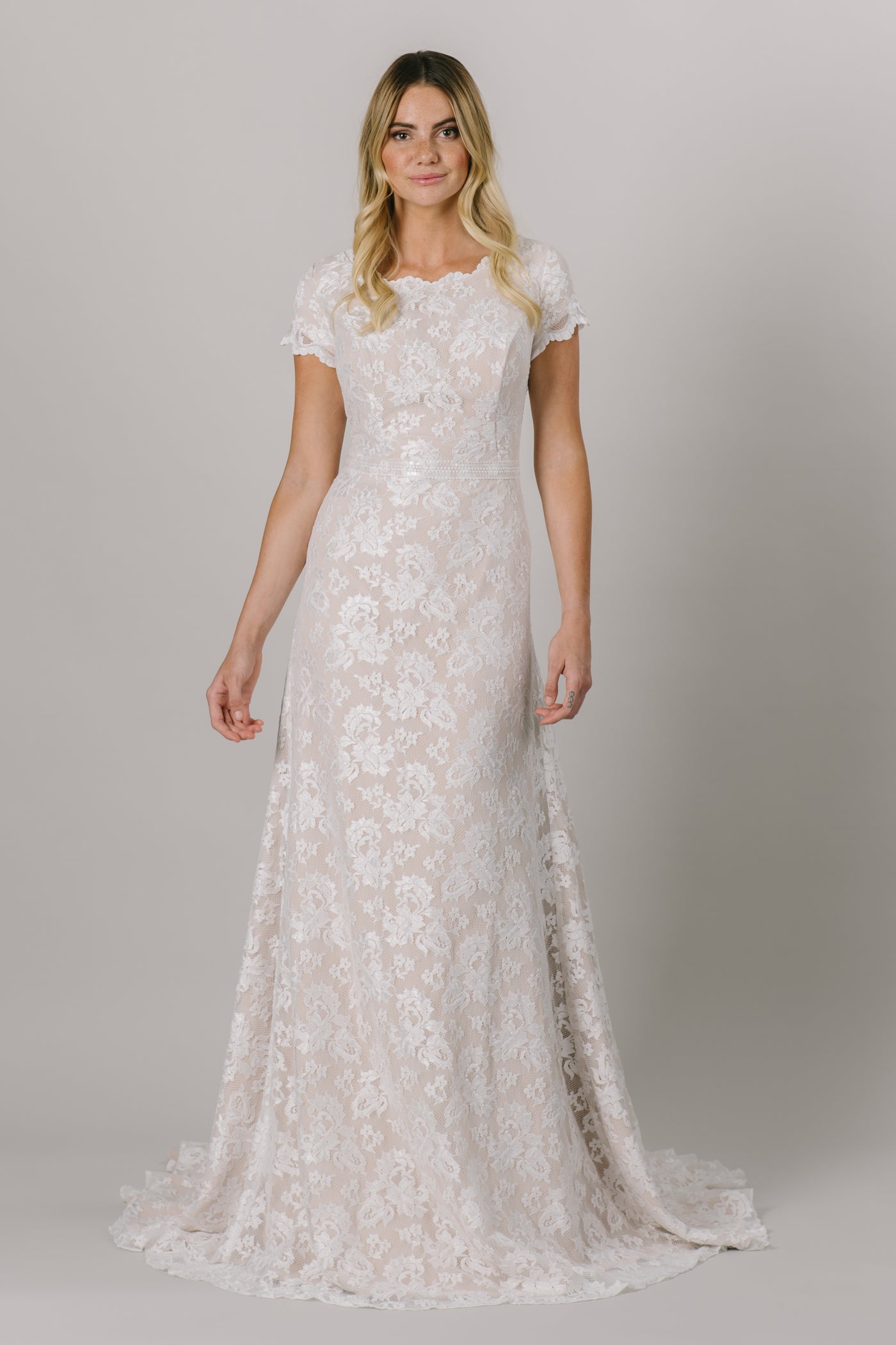 This fitted modest wedding dress is made with a delicate lace pattern and features a fun lace belt. The short illusion sleeves and neckline have the cutest little ruffle. Available in Ivory and Ivory/Cappuccino (as pictured).   ﻿Style Love: This dress is part of our brand new, exclusive LatterDayBride wedding dress collection.