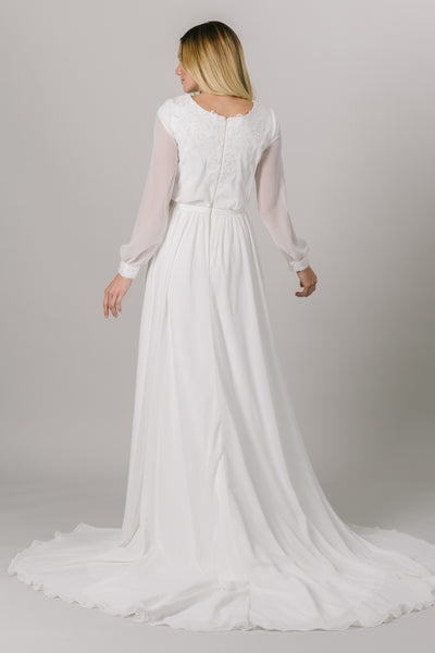 This long-sleeve modest wedding dress features a v-neckline, bishop sleeves, and an a-line fit that flatters every figure.   Style Love: Gorgeous shimmering lace around the neckline and sleeve cuffs! From a bridal store in downtown SLC, Utah.