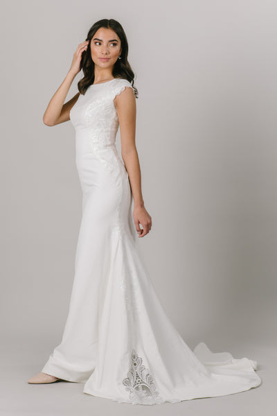 Elegant and simple, this brand new, modest wedding dress features a fitted silhouette and a beautiful lace that trails down either side of the dress.   ﻿Style Love: This dress is part of our brand new, exclusive LatterDayBride wedding dress collection.