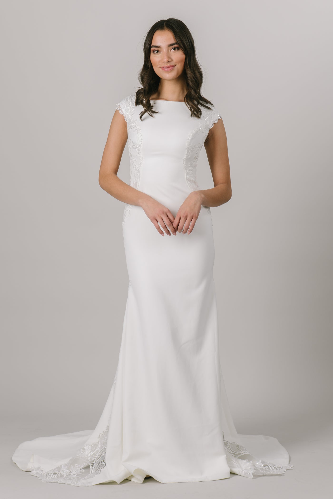 Elegant and simple, this brand new, modest wedding dress features a fitted silhouette and a beautiful lace that trails down either side of the dress. 