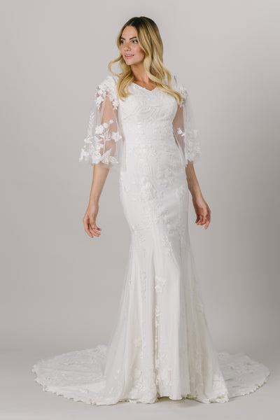 This unique modest wedding gown is like nothing you've seen! It features a v-neckline, fitted silhouette, and gorgeous flowery lace. This gown provides such an amazing fit with details you'll love! Available in Ivory and Ivory/DecoGold. 