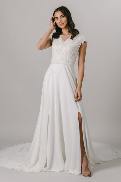 This wedding dress is an A-line fit featuring a beautiful beaded bodice. Complete with a flattering v-neckline and bead belt, this gown also features a fun slit in the front. 