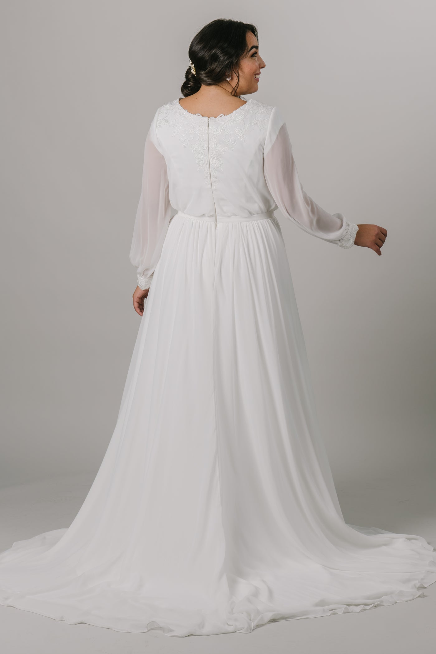 The back of a plus size version long-sleeve modest wedding dress features a v-neckline, bishop sleeves, and an a-line fit that flatters every figure.   Style Love: Gorgeous shimmering lace around the neckline and sleeve cuffs!