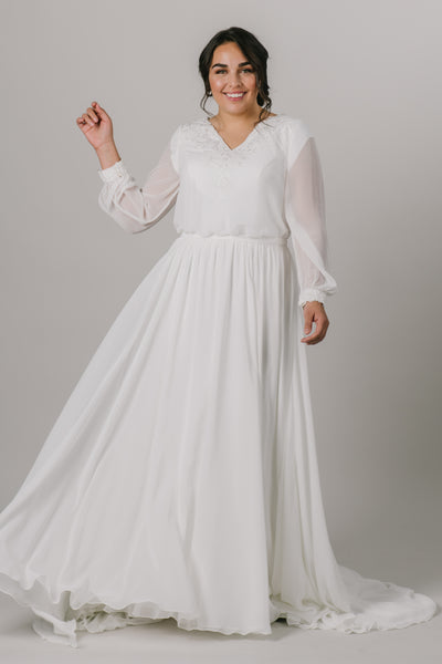 This plus size version long-sleeve modest wedding dress features a v-neckline, bishop sleeves, and an a-line fit that flatters every figure.   Style Love: Gorgeous shimmering lace around the neckline and sleeve cuffs!