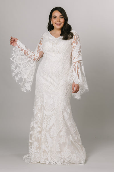 Moments Made Bridal boho styled wedding dress with long trumpet lace sleeves. It has a v-neckline and a fitted silhouette. Sheet lace covers the dress. This modest wedding dress is perfect for any wedding season.