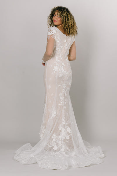 A back view of a modest wedding dress with illusions sleeves and a floral pattern with leaves and a seamless zipper. 